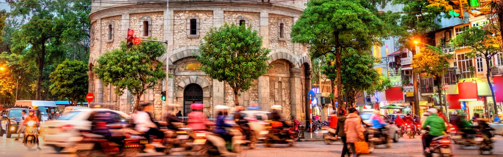 A motion-blur photo of cars and motorcycles driving down a busy, tree-lined street.